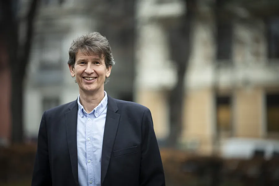 Smilende mann med mørkt hår og dressjakke. Foto.